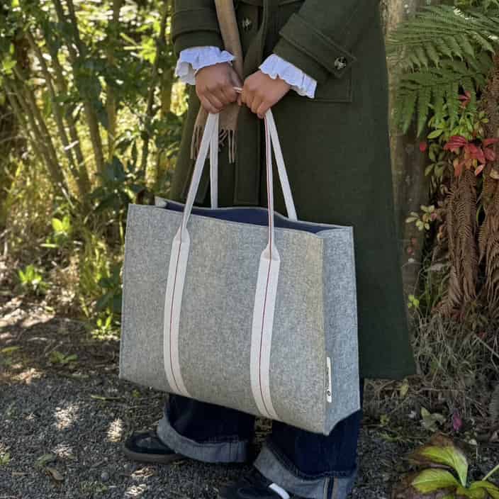 Person holding a gray tote bag with white straps outdoors