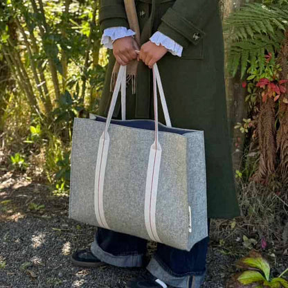 Person holding a gray tote bag with white straps outdoors