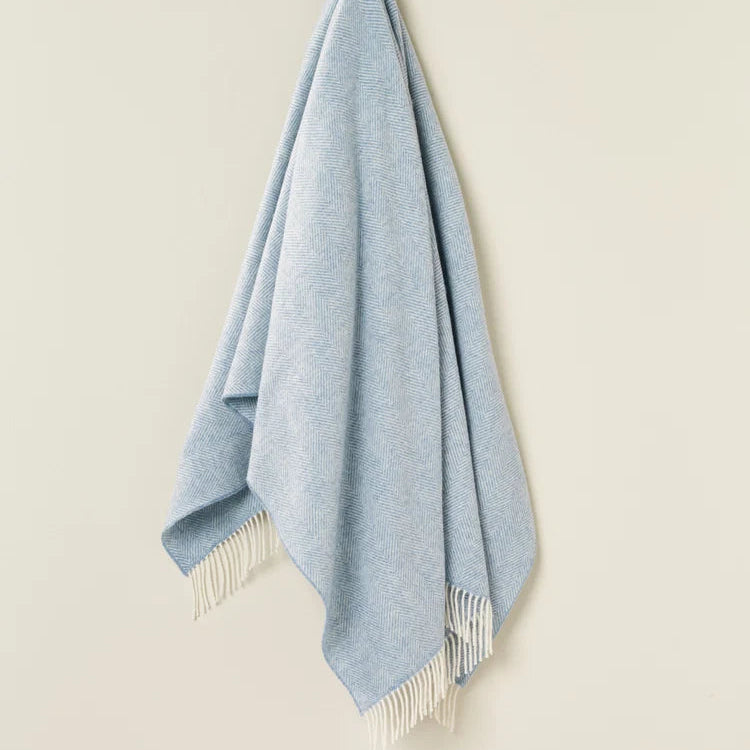 Light blue throw blanket with white fringe on a beige background