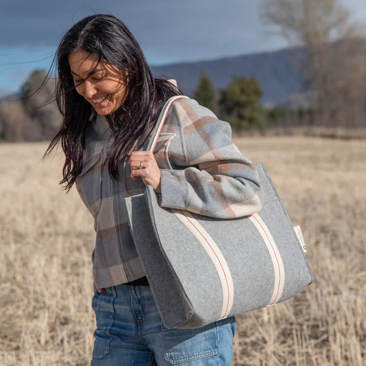 Woman holding a large gray tote bag in an outdoor setting with mountains in the background