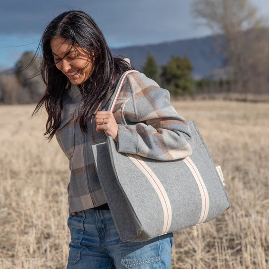 Woman holding a large gray tote bag in an outdoor setting with mountains in the background