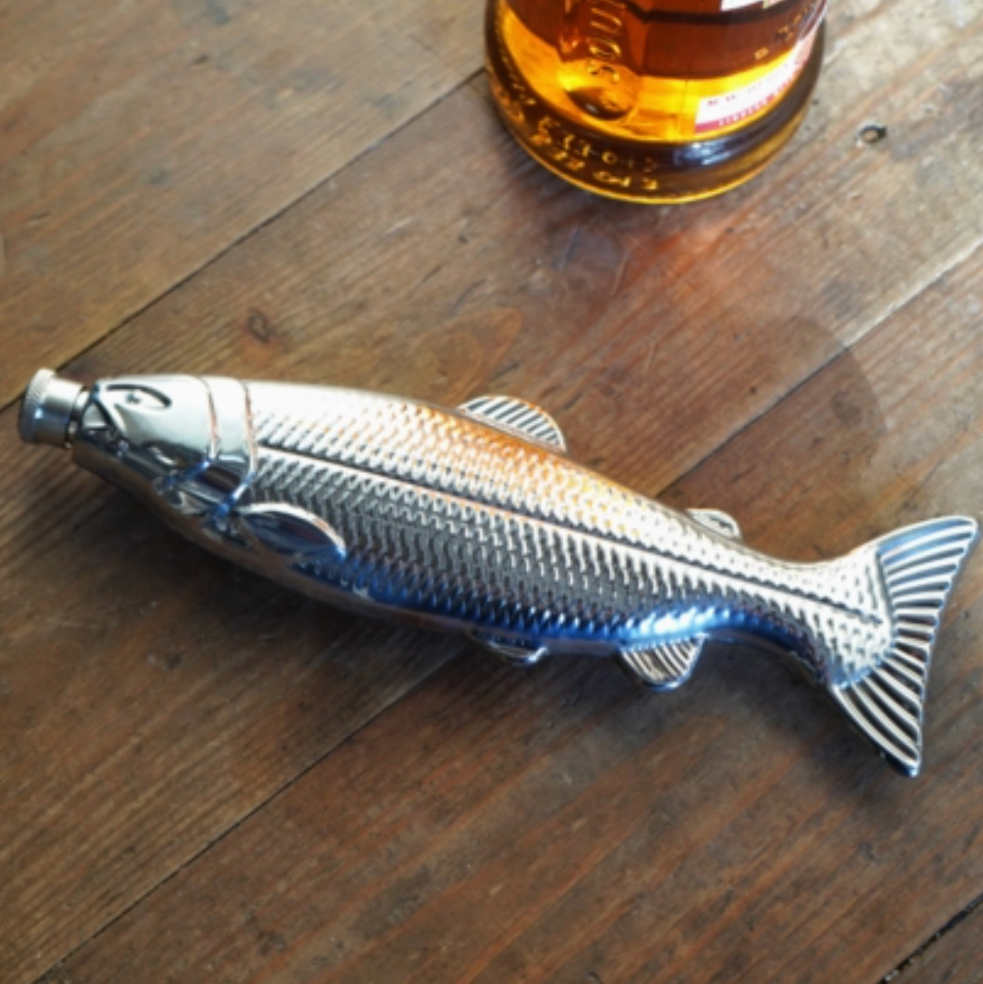 Fish-shaped bottle opener on a wooden surface with a bottle in the background