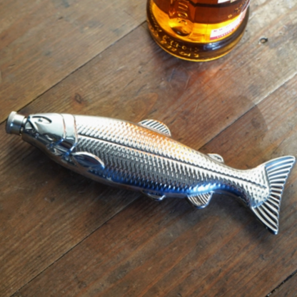 Fish-shaped bottle opener on a wooden surface with a bottle in the background