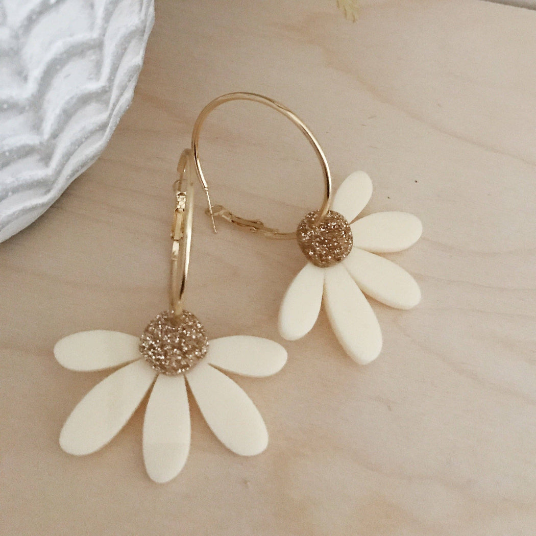 White flower-shaped earrings with gold centers on a light wooden surface.