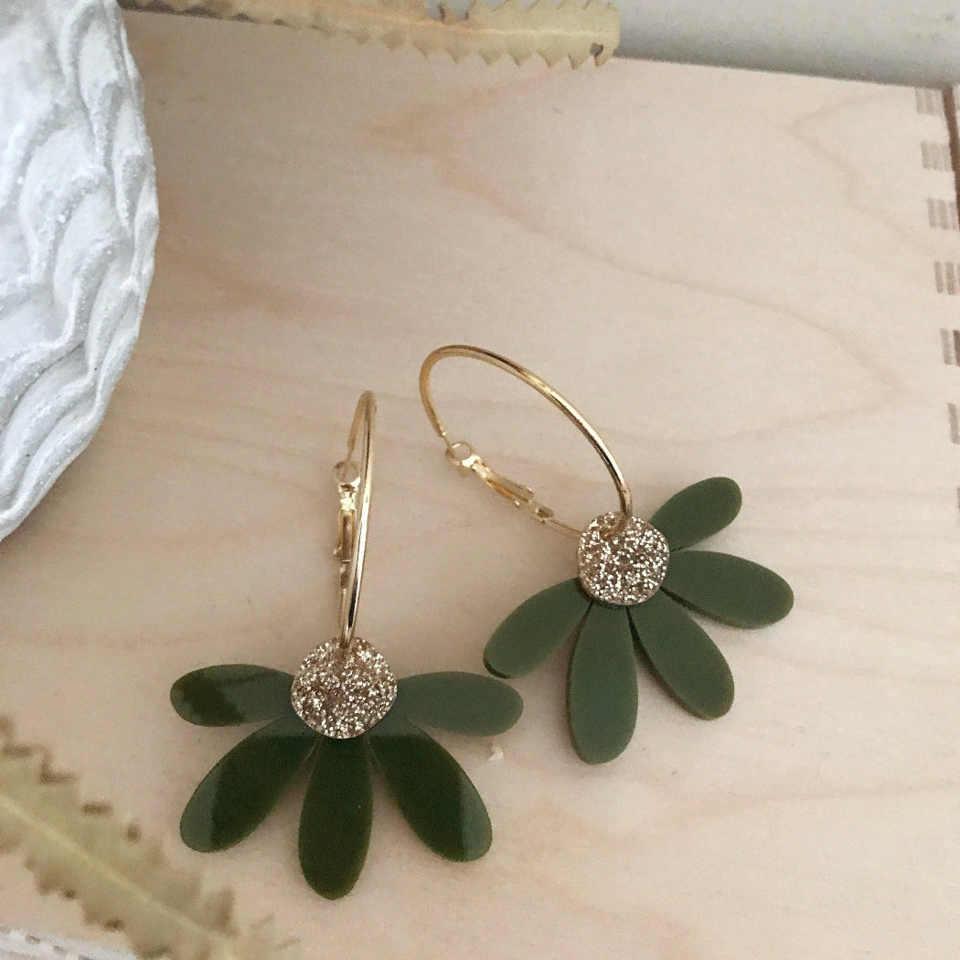 Green floral earrings with golden glitter centers on a textured surface