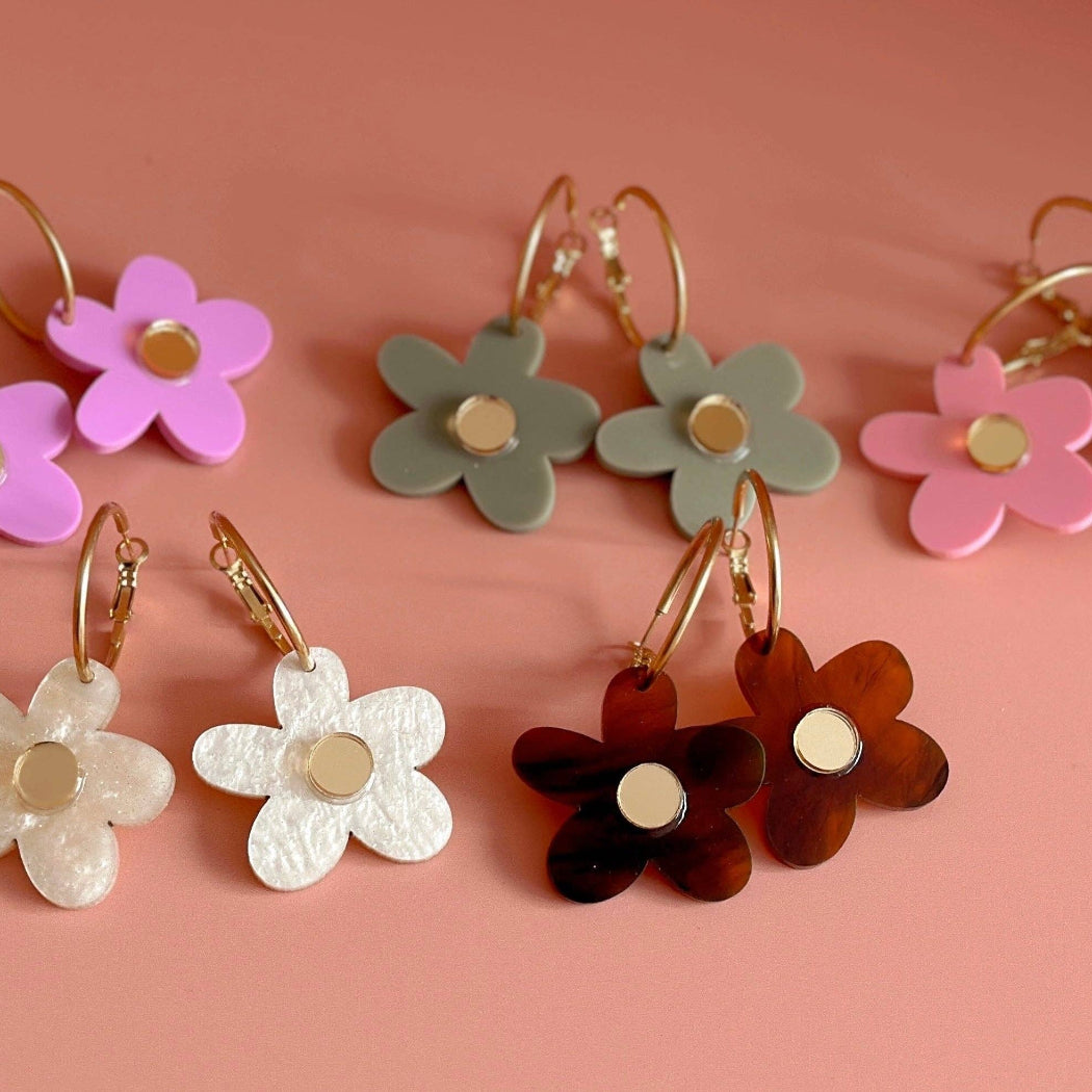 Set of colorful flower-shaped earrings on a pink background