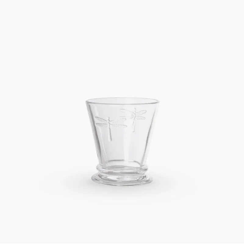 A clear glass tumbler with a dragonfly motif etched on the front, set against a solid white background.