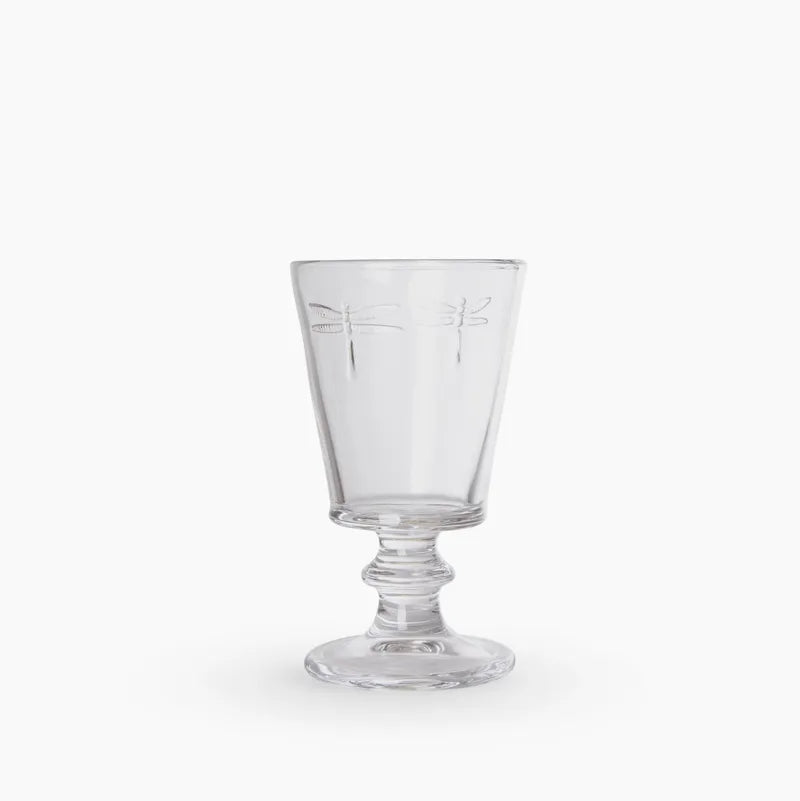 A clear glass goblet with a decorative stem, featuring an etched dragonfly motif on the upper half, set against a plain white background.