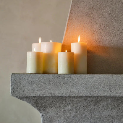Five cream-colored pillar candles, arranged on a textured gray stone mantelpiece against a warm beige plaster wall.