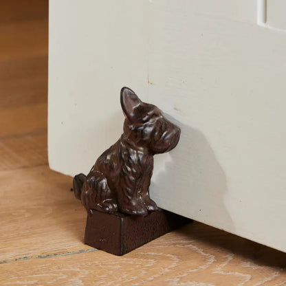 Decorative brown metal dog-shaped door stopper on a wooden floor.