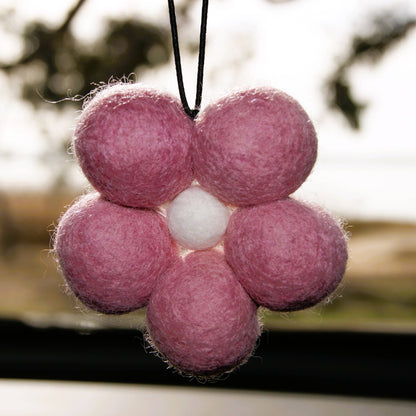 Pink felt flower ornament with a white center against a blurred natural background