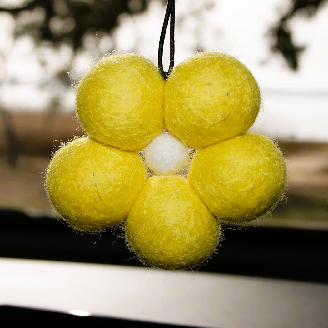 Yellow felt ball ornament with a white center hanging outdoors.