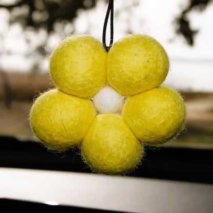 Yellow felt ball ornament with a white center hanging outdoors.