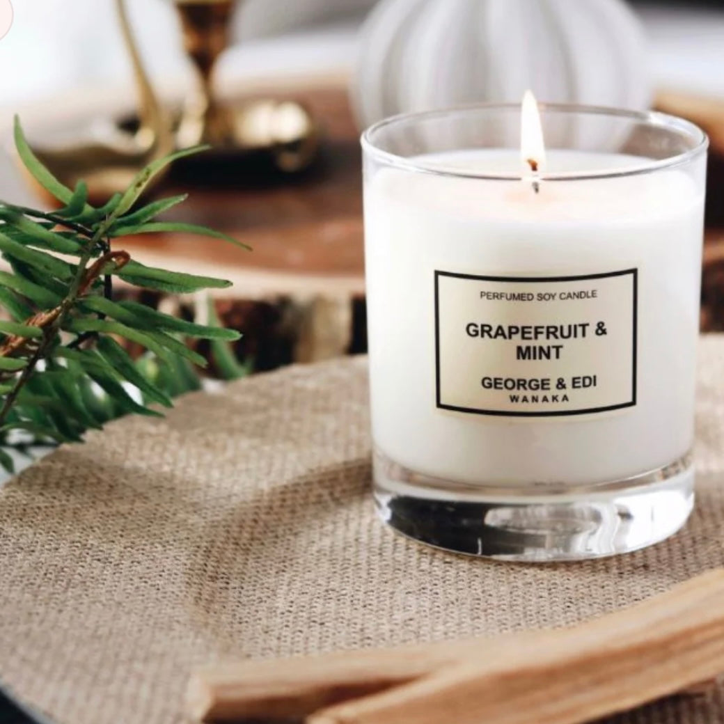 Candle labeled 'Grapefruit & Mint' by George & Edi on a textured surface with greenery.