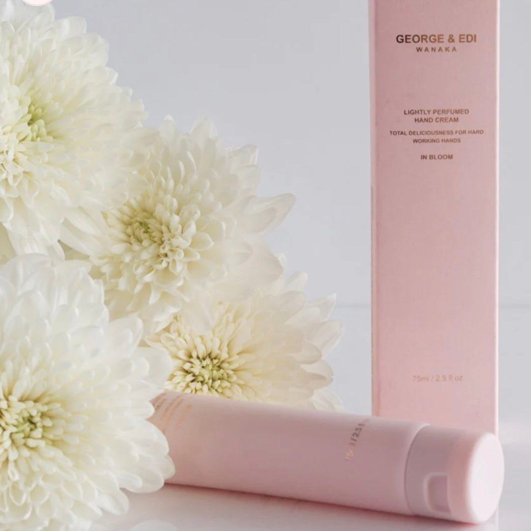 Pink hand cream and packaging with white flowers on a light gray background