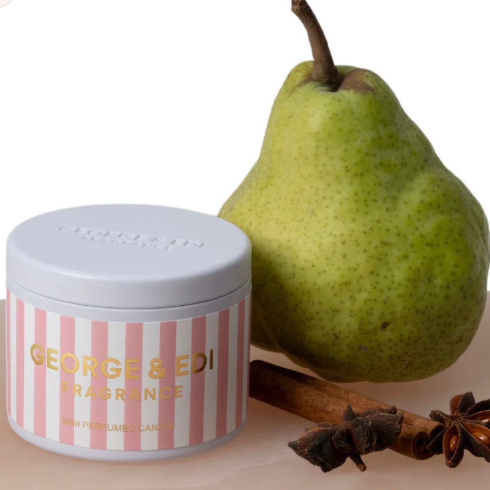Candle with striped design and 'George & Edi' branding next to a green pear and cinnamon stick on a white background