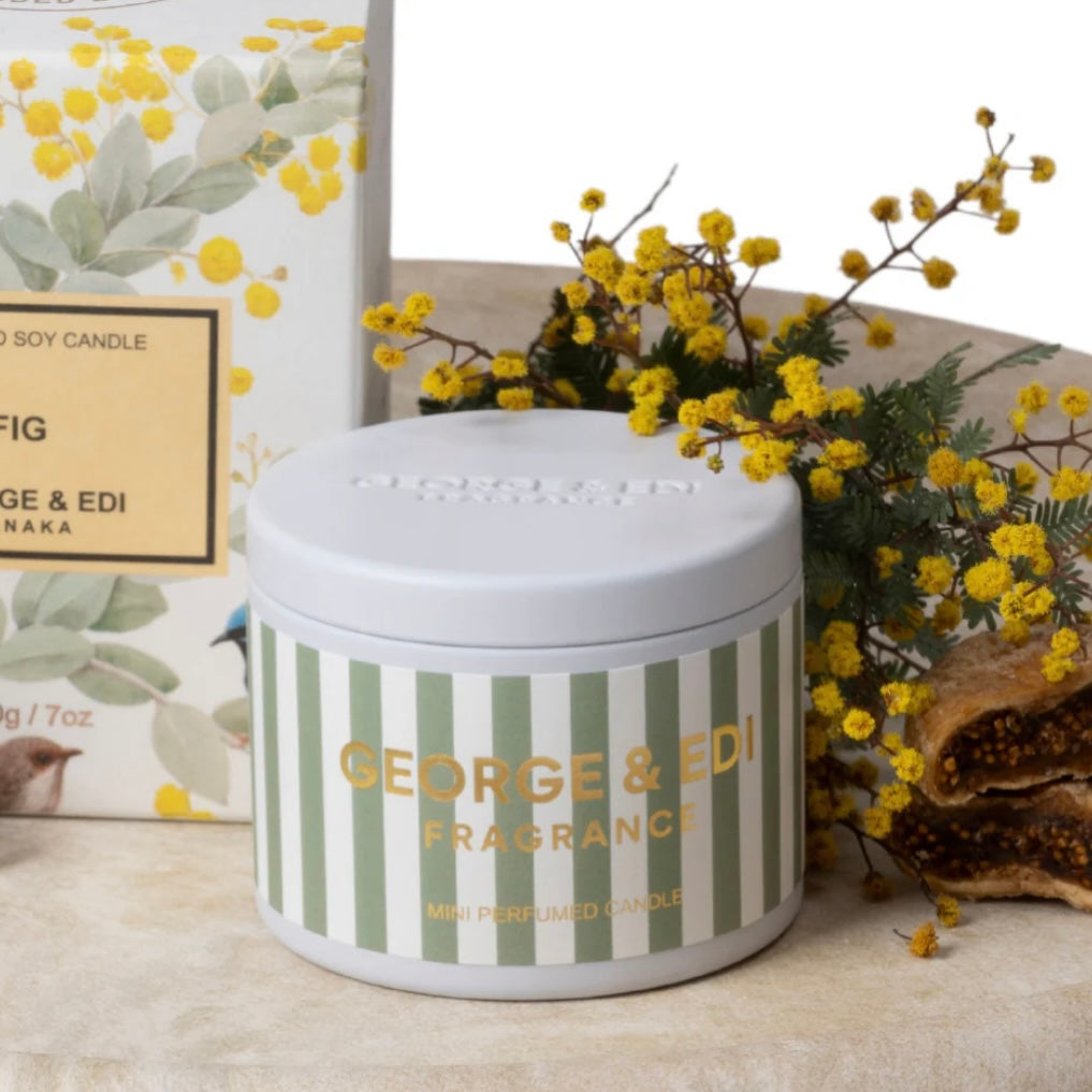 Candle jar with striped design and 'George & Edi' branding, surrounded by yellow flowers and a box.