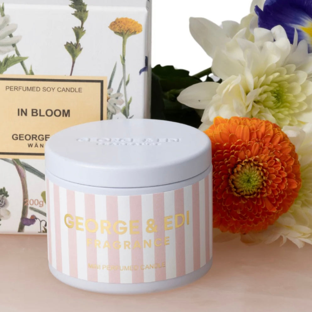 Candle jar with 'George & Edi Fragrance' branding surrounded by flowers