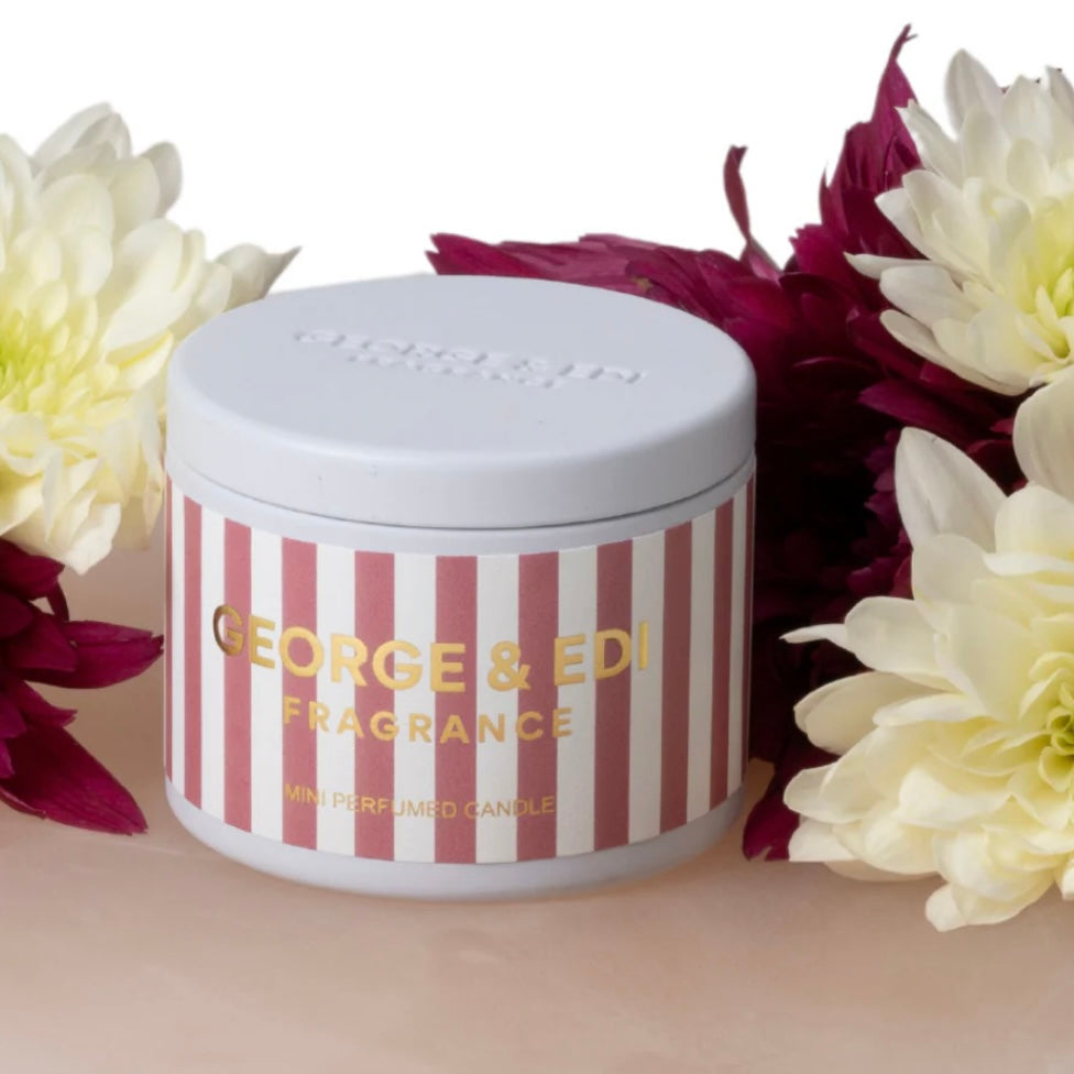 Striped candle with 'George & Edi Fragrance' branding surrounded by flowers