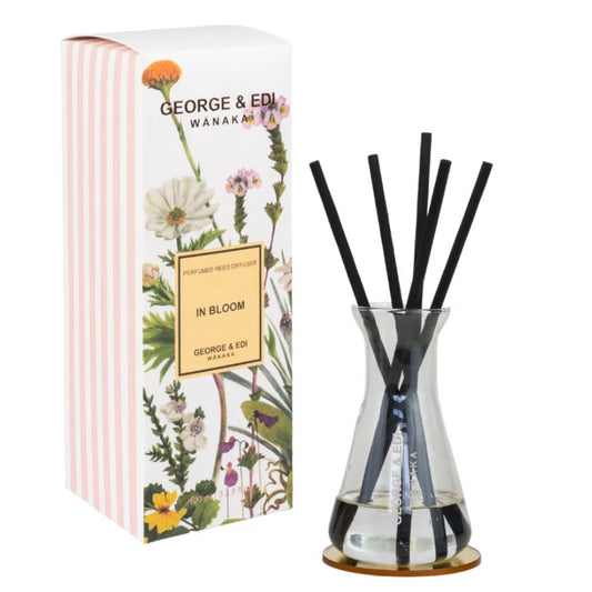 Diffuser set with black sticks in a clear vase next to its packaging featuring floral designs.