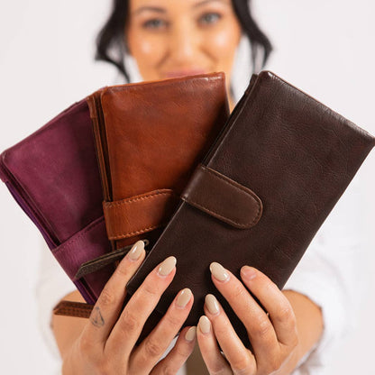 Woman holding three leather wallets of different colors against a plain background