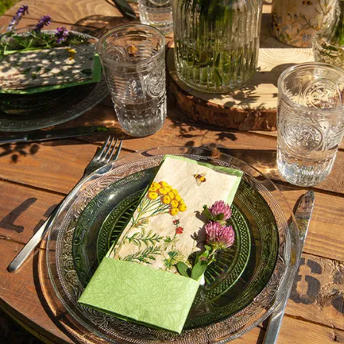 Table setting with green plates, glasses, and a floral napkin on a wooden table.