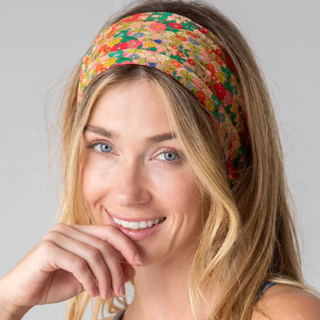 A smiling blonde woman wearing a colorful floral patterned headband and a matching patterned top, photographed against a plain light gray studio background.