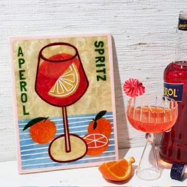 Aperol Spritz bottle with a glass of cocktail and oranges on a wooden surface.