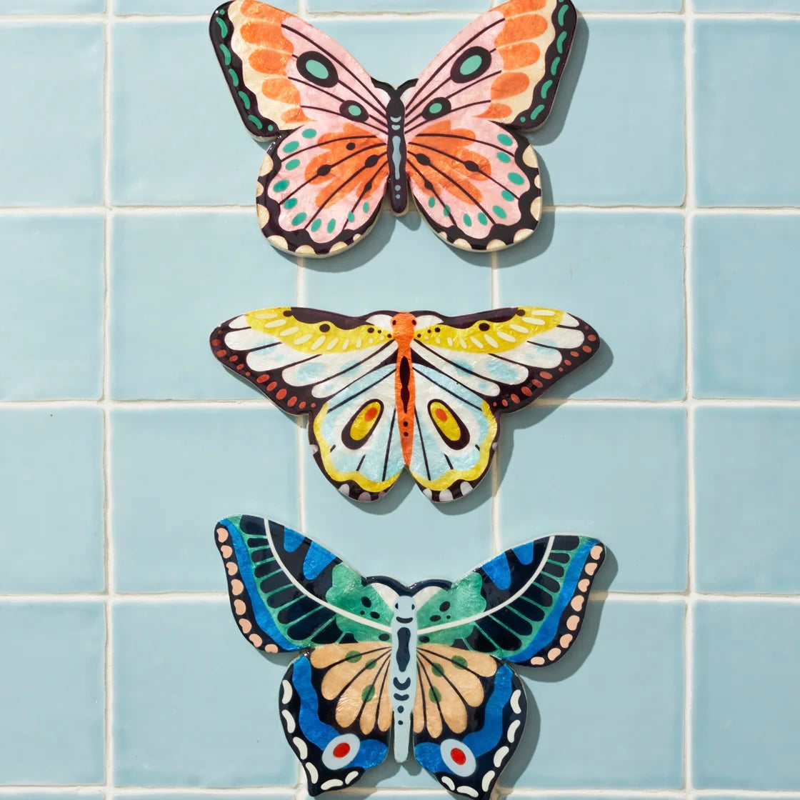 Three colorful butterfly-shaped decorations on a blue tiled wall.