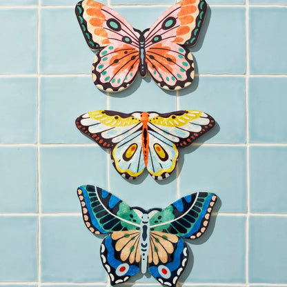 Three colorful butterfly-shaped decorations on a blue tiled wall.