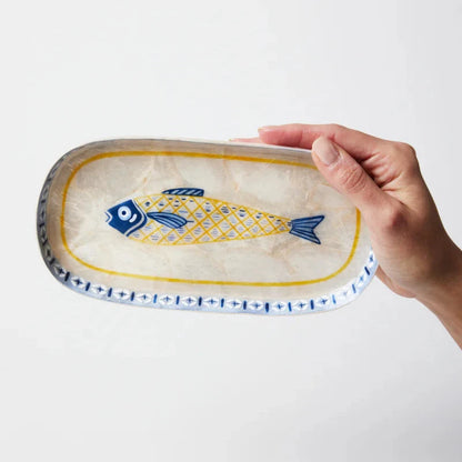 Hand holding a decorative ceramic plate with a fish design on a white background
