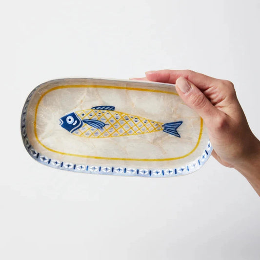 Hand holding a decorative ceramic plate with a fish design on a white background