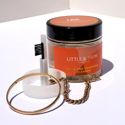 Jar of 'Little & Stone' product with a brush and gold ring on a white surface