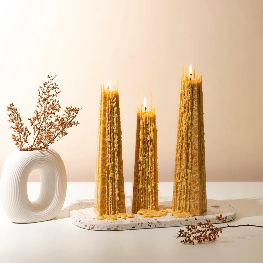 Three tall, textured candles on a decorative stand with a vase and dried flowers on a light background