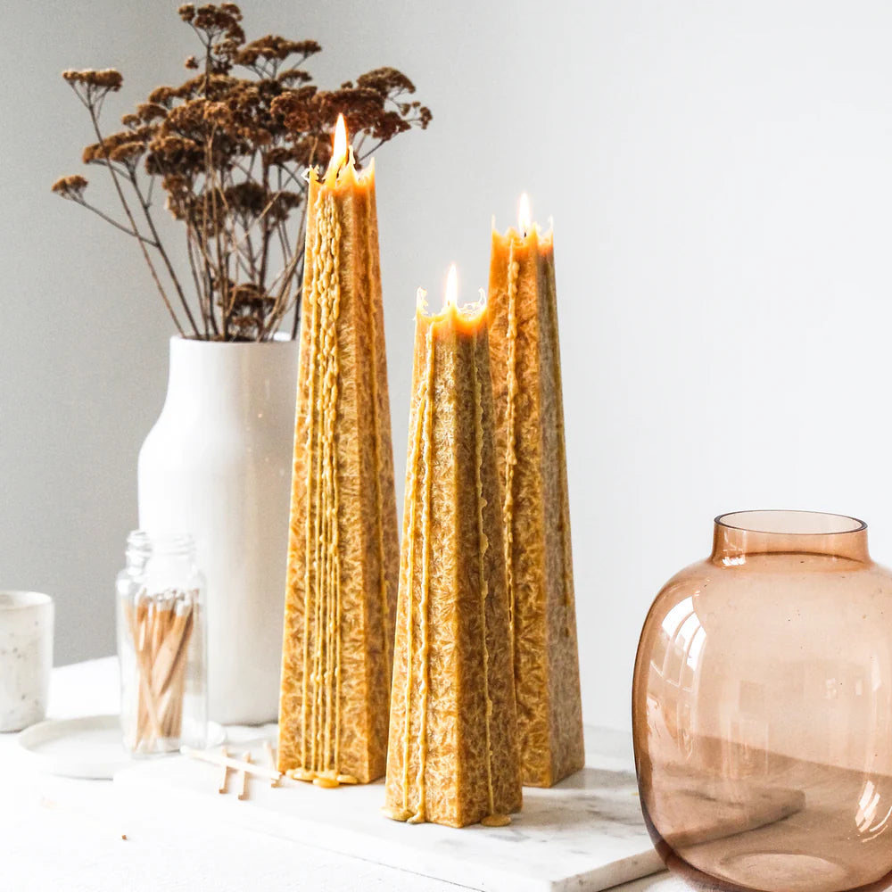 Three tall, textured candles on a white surface with decorative items like a vase and dried flowers.