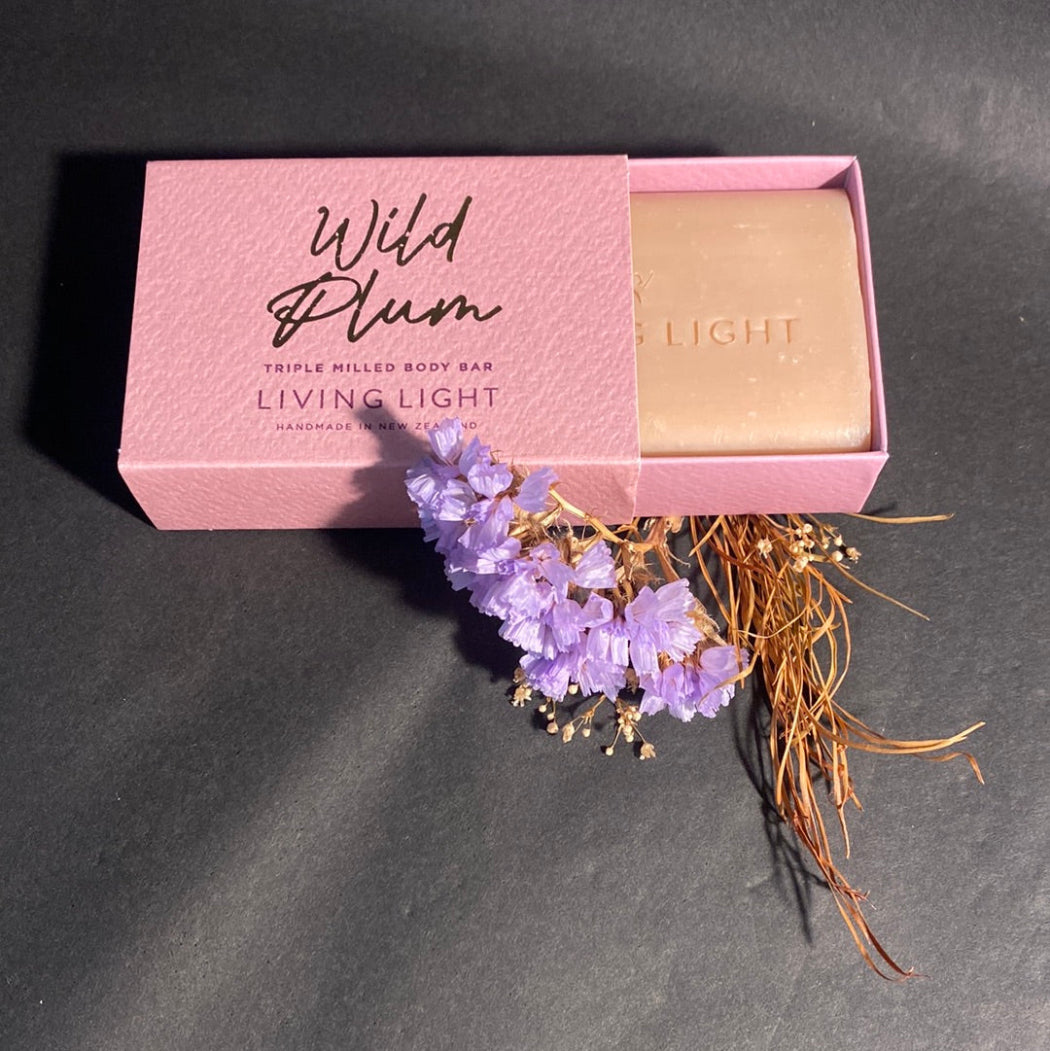 Pink box of 'Wild Plum' soap with a bar of soap inside, accompanied by dried flowers on a dark background.