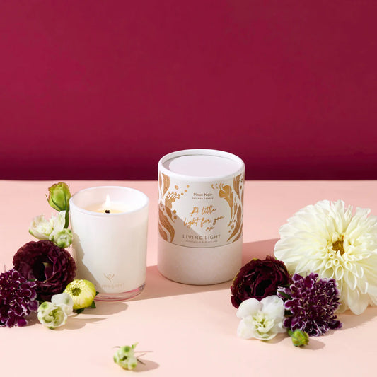 Candle and decorative container with flowers on a pink surface against a red background