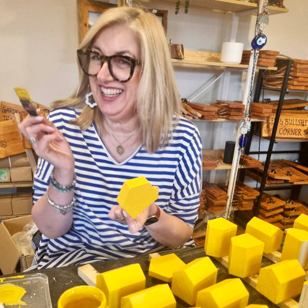 Woman holding a yellow object in a workshop setting with shelves in the background