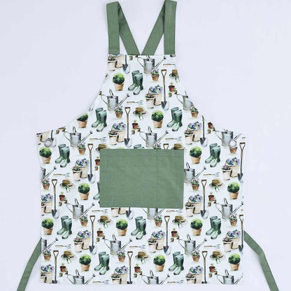 A white apron with an all-over gardening-themed print of pots, plants, gloves, and tools, featuring solid sage green straps and a large solid sage green front pocket. The apron is laid flat against a light gray background.