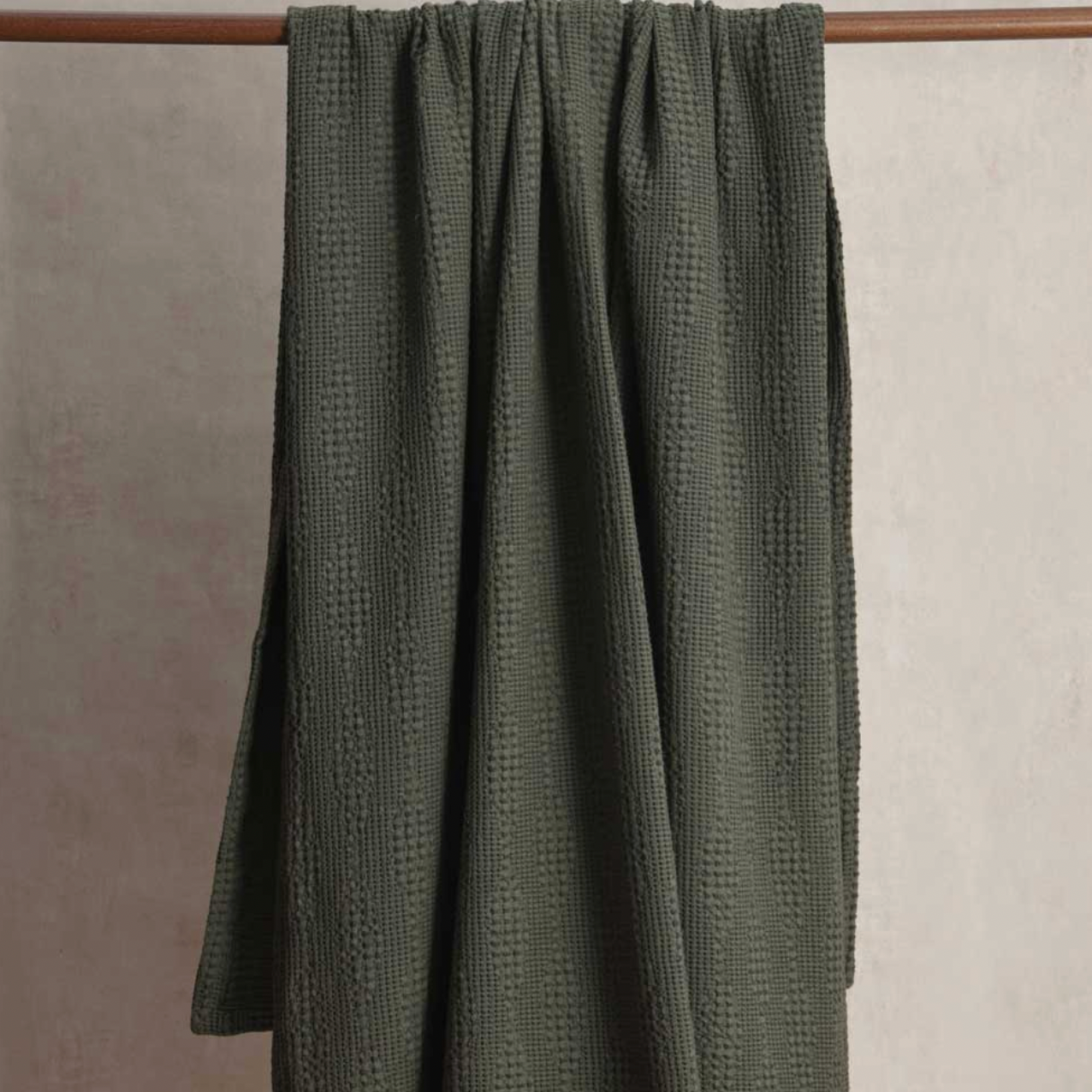 Green textured fabric draped over a wooden rod against a beige wall.
