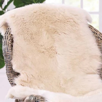 A beige sheepskin rug placed on a wicker chair, showcasing its soft and fluffy texture.