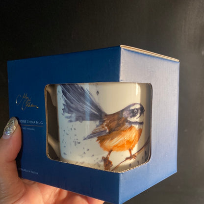 A hand holding a Meg Hawkins designed fine bone china mug with a bird illustration, packaged in a blue window gift box.