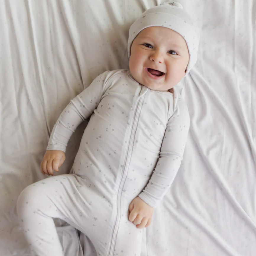 Baby in a white outfit with a matching hat lying on a white blanket