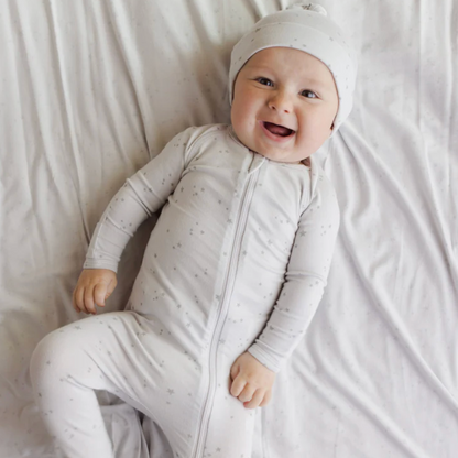Baby in a white outfit with a matching hat lying on a white blanket
