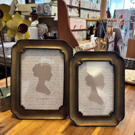 Two ornate gold photo frames displayed on a table, one small and one medium sized, with a silhouette of a female figure within the frames.