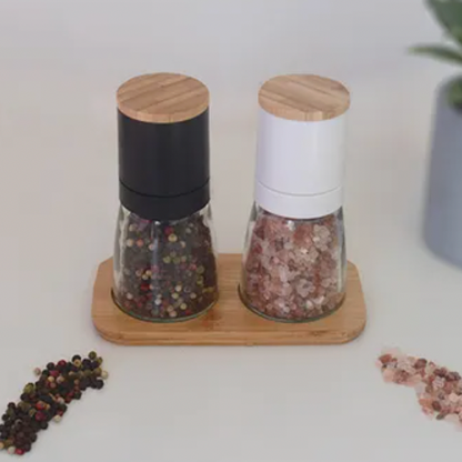 Two pepper grinders on a wooden stand with scattered peppercorns on a white surface.