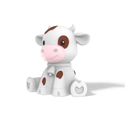 A cute, stylized 3D cartoon cow figurine sitting down. The cow is primarily white with brown spots, a pink snout, and a small white scarf, set against a plain white background with a soft shadow.
