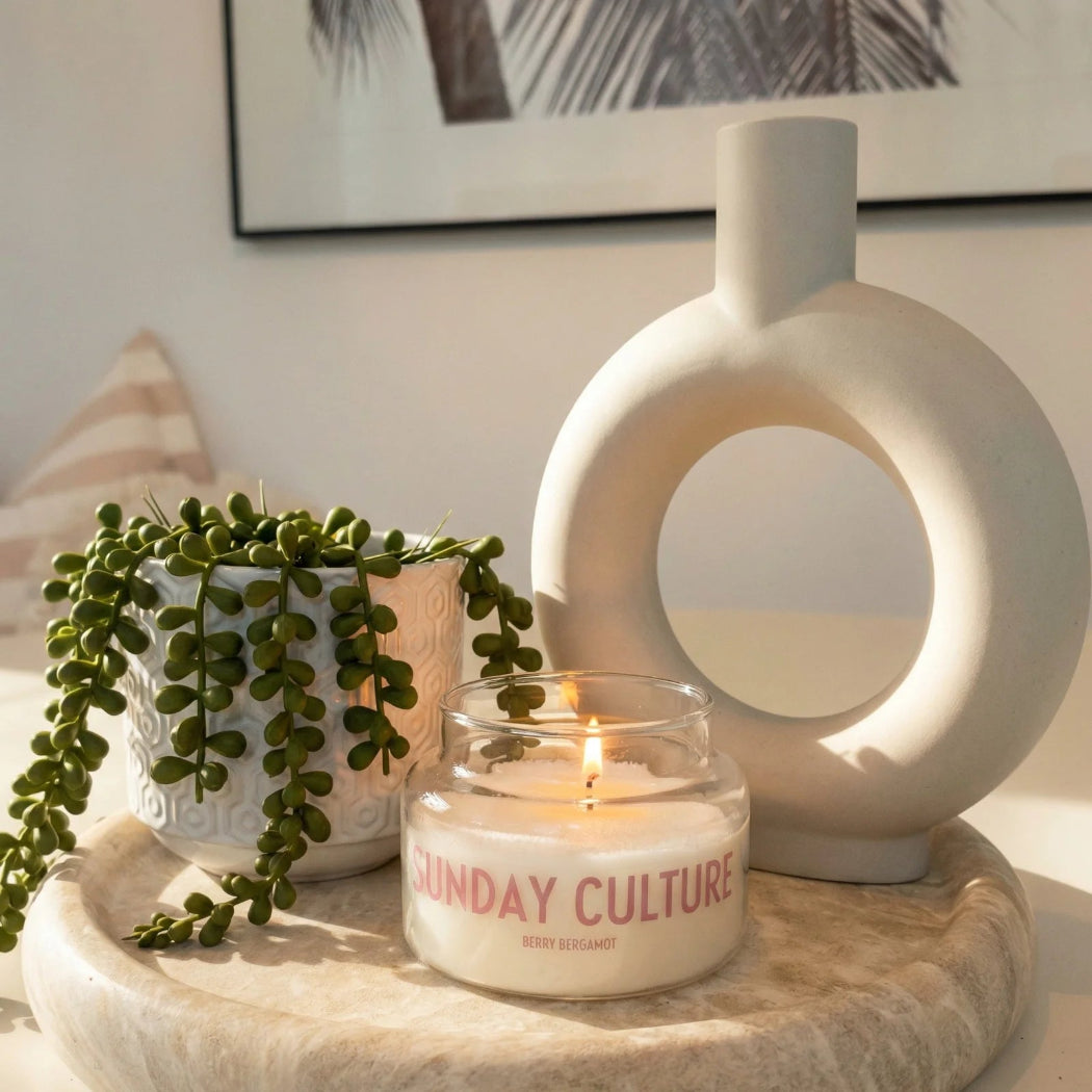 Candle with 'Sunday Culture' branding on a decorative surface with a plant and vase.