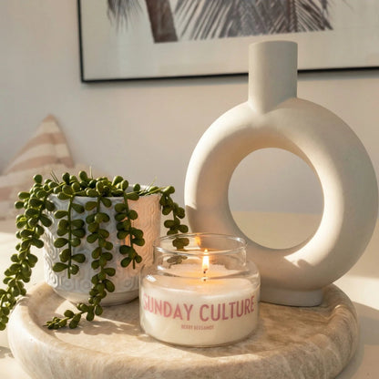 Candle with 'Sunday Culture' branding on a decorative surface with a plant and vase.