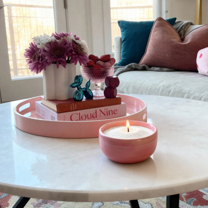 Pink candle on a coffee table with decorative items and a couch in the background